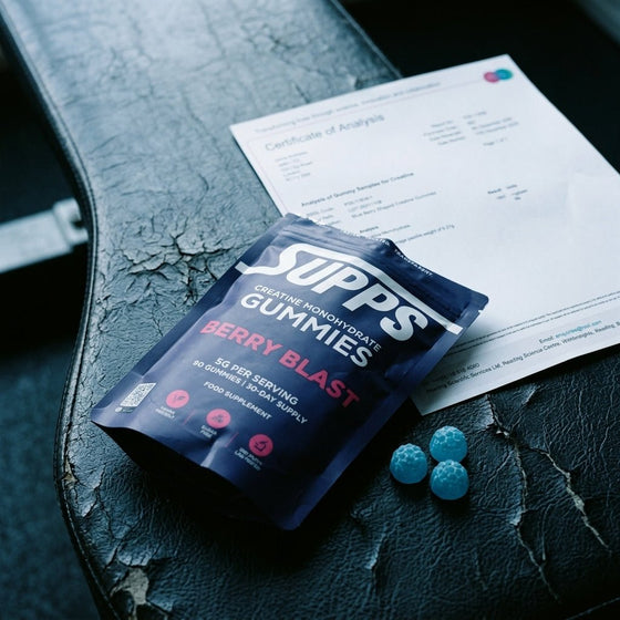 Supps Berry Blast creatine gummies pouch resting on a lab Certificate of Analysis document with three gummies beside it