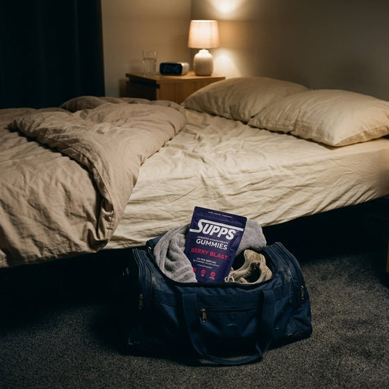 Supps Berry Blast creatine gummies pouch in an open gym bag at the foot of a bed in a dimly lit bedroom