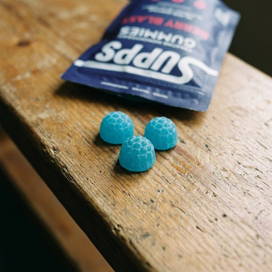 Close-up of three Supps Berry Blast creatine gummies on a wooden bench next to the pouch